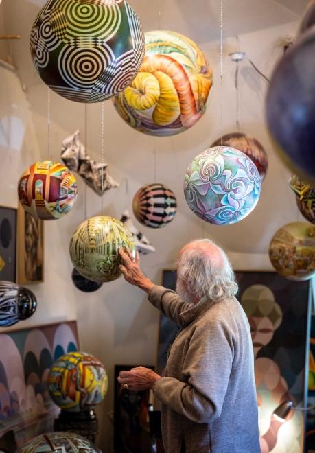 man reaching out to touch an artistic globe shaped piece of artwork hanging from the ceiling